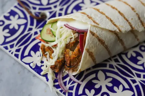 Domowy kebab zawinięty w tortillę z warzywami i sosem na ozdobnym talerzu.