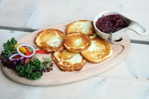 Smażony oscypek z żurawiną, podany z sałatką i pieczywem, na drewnianej desce.