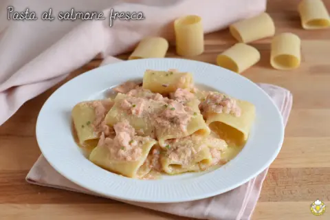 Piatto di paccheri conditi con un cremoso sugo di pasta al salmone fresco, guarnito con erba cipollina.