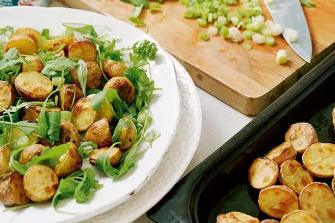 En härlig rostad potatissallad med ruccola och salladslök, redo att serveras.