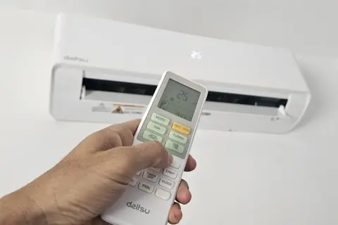 Mano ajustando el control remoto del aire acondicionado para cambiar la temperatura. La pantalla muestra 25.5°C.