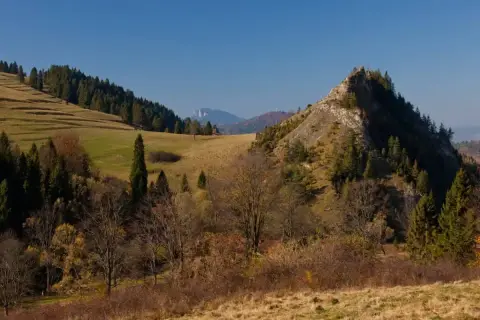 Jesienny krajobraz z dominującą, skalistą górą wysoką. Na zboczach drzewa iglaste i liściaste w jesiennych barwach.