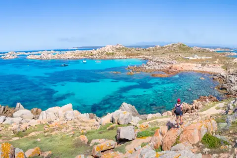 Vue panoramique de l'île Lavezzi, avec ses eaux turquoise cristallines, ses rochers granitiques et une randonneuse admirant le paysage.