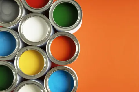 Un assortiment de pots de peinture glycero ou acrylique ouverts, révélant des couleurs vives comme le bleu, le jaune, le rouge, le vert et l'orange sur fond orange.