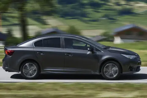 Ciemnoszara Toyota Avensis 2.0 D4D w ruchu, z rozmytym tłem górskiego krajobrazu.