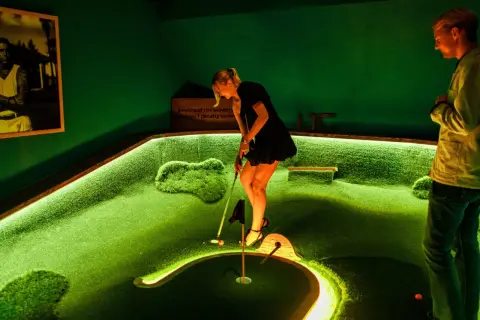 En kvinna spelar minigolf på en bana i Slottskogen. En man tittar på.