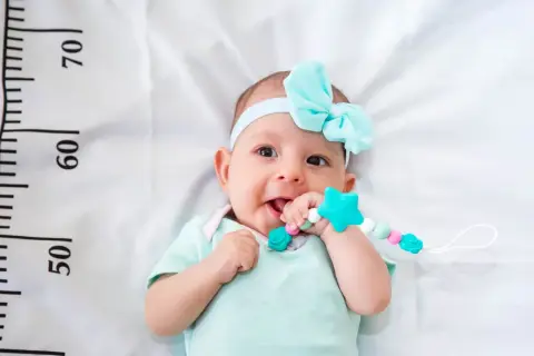 Bebé con diadema azul y mordedor, cerca de una cinta métrica que indica el percentil 15.