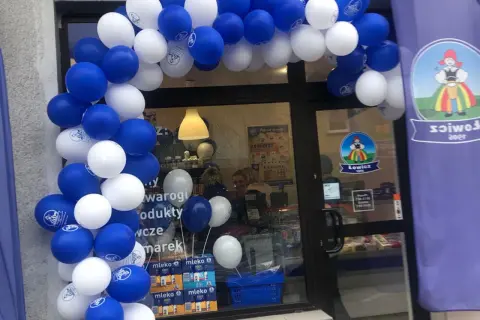 Biało-niebieskie balony tworzą łuk nad wejściem do sklepu z logo Łowicz.
