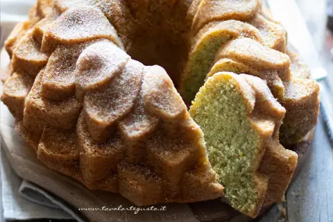 Una deliziosa torta al pistacchio, soffice e profumata, cosparsa di zucchero a velo. La fetta rivela il suo colore verde brillante.