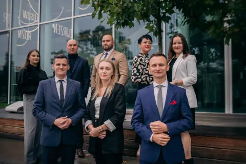 Grupa profesjonalistów w garniturach i eleganckich strojach pozuje przed nowoczesnym budynkiem.