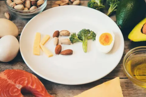 Litery KETO ułożone z sera, orzechów, brokuła i jajka. Czy dieta keto jest zdrowa? Obok łosoś, awokado, oliwa.
