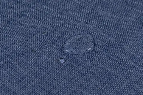 Gocce d'acqua su tessuto blu, dimostrando l'efficacia del lavaggio antimacchia in lavatrice.
