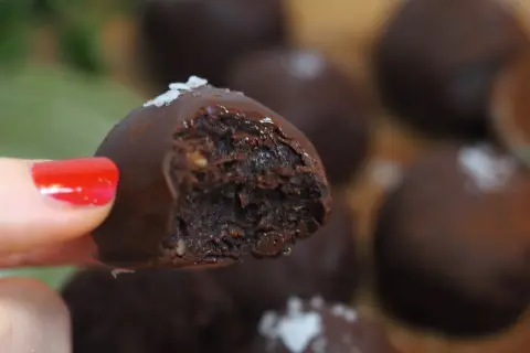 En hand med rött nagellack håller en chokladpralin med dadelfyllning. Perfekt för att baka med dadlar!