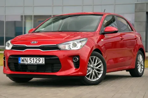 Czerwone Kia Rio przed budynkiem. Wymiana żarówki do jazdy dziennej w tym modelu jest prosta.