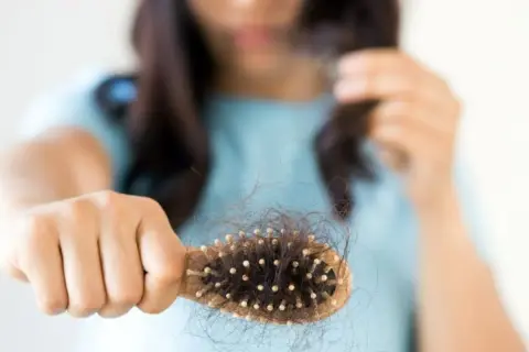 Mujer preocupada por la caída de pelo postparto, mostrando un cepillo lleno de cabello.