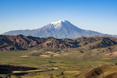 Majestatyczny masyw wulkaniczny w Turcji, Ararat, góruje nad zieloną doliną z polami uprawnymi i krętą drogą.