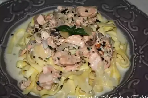 Tagliatelles onctueuses au saumon, parsemées d'herbes fraîches et de poivre noir, servies dans une assiette décorative. Un délice pour les yeux et les papilles.