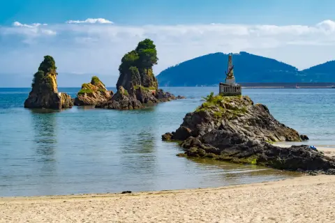 Rocas emergiendo del mar azul, un monumento en una de ellas, y la arena dorada de las playas cerca de Viveiro.