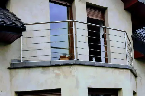 Nowoczesna poręcz ze stali nierdzewnej na balkonie, z widokiem na okna i dachówki.