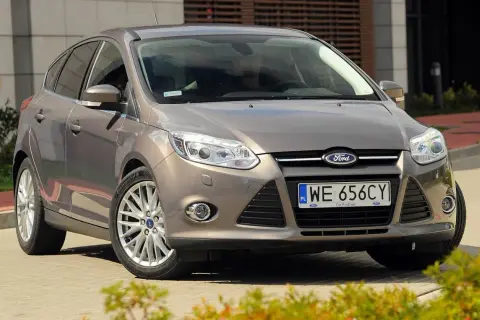 Brązowy Ford Focus MK3, często chwalony w opiniach, prezentuje się elegancko na tle nowoczesnego budynku.