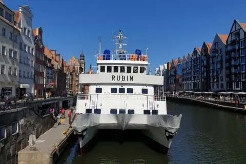Biały prom "Rubin" cumuje w Gdańsku, gotowy do rejsu na Hel. W tle malownicza starówka i kanał.