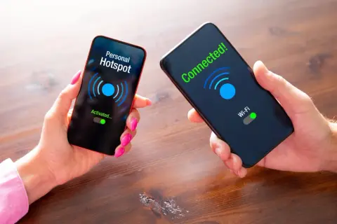 Dwie dłonie trzymają telefony. Na jednym ekranie "Personal Hotspot Activated...", na drugim "Connected! Wi-Fi". Pokazuje, jak udostępnić internet z telefonu.