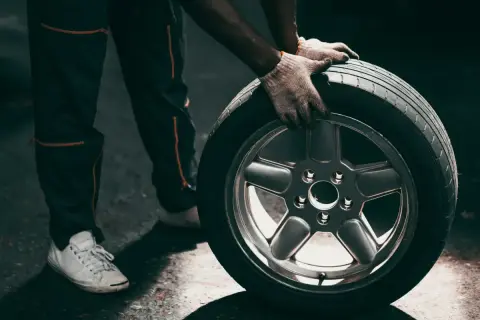 Mechanik w rękawiczkach trzyma koło z felgą, gotowy do wymiany przebitej opony.