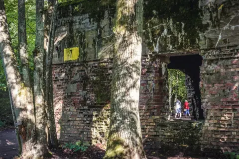 Ruiny Wilczego Szańca porośnięte mchem i drzewami. Dwie osoby wchodzą do ciemnego tunelu.