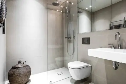 Moderno bagno senza finestra con doccia a filo pavimento, WC sospeso, lavabo minimalista e cesto in vimini.