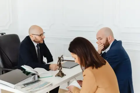 Prawnik omawia z parą kwestie spadkowe. Mężczyzna zasłania usta, być może zaskoczony treścią testamentu.