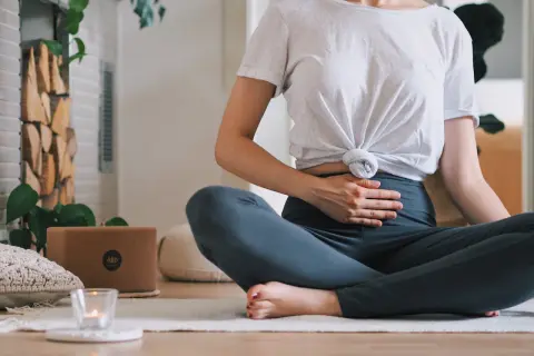 Frau in Lotussitz übt Kapalabhati Pranayama, Hände auf dem Bauch, um die Bauchatmung zu spüren.