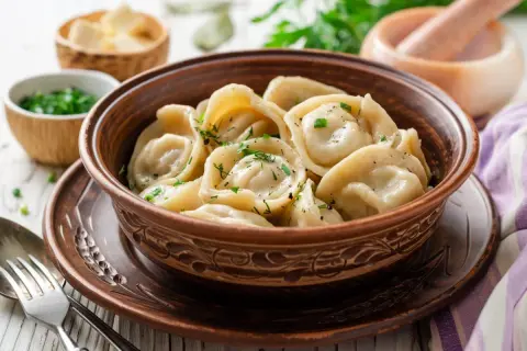 Pielmieni co to? To pyszne, ręcznie robione pierożki, gotowane i posypane świeżymi ziołami, podane w glinianej misce.