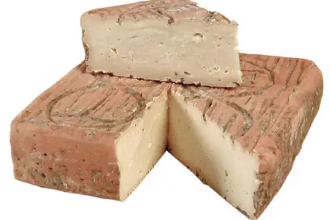 Un pezzo di taleggio bergamasco, con la crosta rosata e la pasta chiara e compatta, tagliato a spicchi.