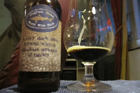 Una bottiglia e un bicchiere di Dogfish Head World Wide Stout, una birra scura con un significato di abbondante orzo.