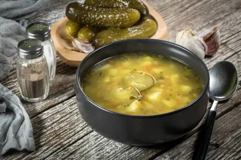Miseczka zupy ogórkowej, obok miseczka z ogórkami kiszonymi i przyprawy. Czy zupę ogórkową się zagęszcza?