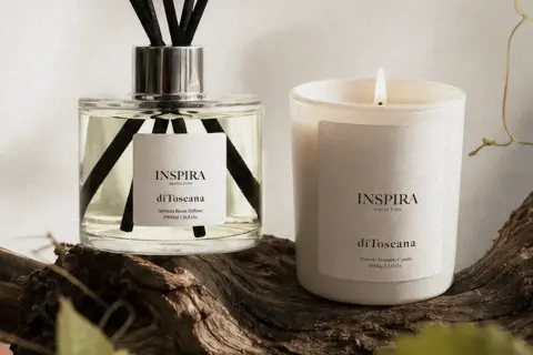 Dyfuzor i świeca Inspira "di Toscana" na tle drewna. Te zapachy tworzą własne, piękne histoires de parfums.