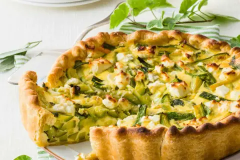 Tarte ricotta courgette dorée, garnie de dés de fromage blanc et de lamelles de courgettes vertes.