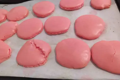 Coques de macarons roses sur une plaque de cuisson. Certaines sont parfaites, d'autres craquent, illustrant pourquoi les macarons craquent.
