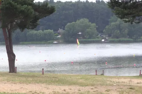 Pławniowice jezioro: wiatr napędza żaglówkę, a na brzegu widać piaszczystą plażę i drzewa.
