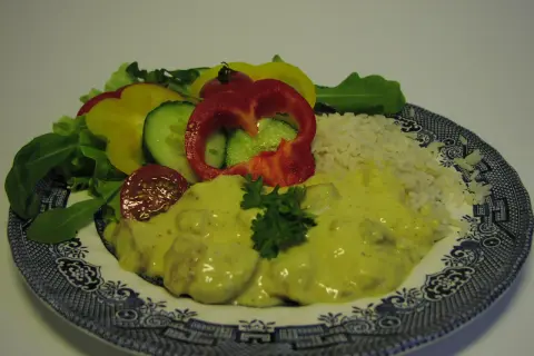 En tallrik med kyckling curry, ris och en sallad av paprika, gurka och tomat.