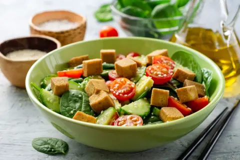 Pyszna sałatka z tofu, pomidorkami koktajlowymi, ogórkiem i szpinakiem, posypana sezamem. Idealna na lekki posiłek.