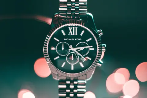 Elegancki zegarek Michael Kors z ciemną tarczą i srebrną bransoletą, na tle rozmytych świateł.