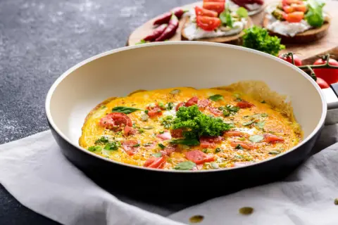 Omlet z pomidorami i ziołami na patelni. Idealny pomysł, jak ograniczyć węglowodany w diecie.