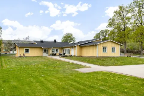Gult behandlingshem för vuxna med gräsmatta och träd.