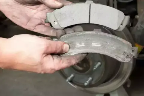 Mani sporche confrontano pastiglie freni nuove e usurate, mostrando il **spessore minimo pastiglie freni** raggiunto da quelle vecchie.