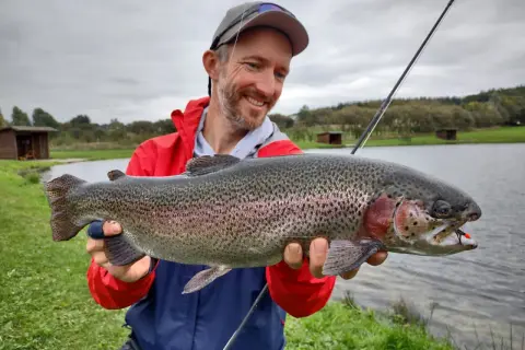 Glücklicher Angler hält stolz einen großen Regenbogenforelle, ein toller Fang beim LImfjord angeln.
