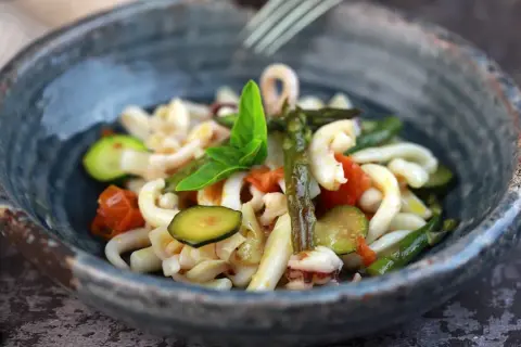 Deliziosa insalata di mare con verdure fresche: calamari, pomodorini, zucchine e asparagi, guarnita con basilico.