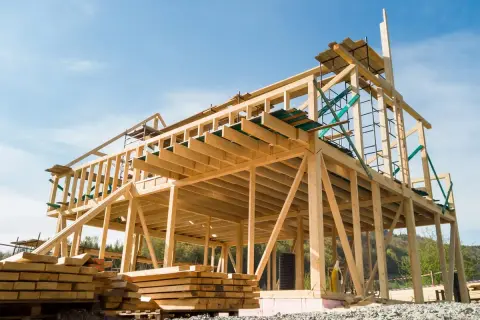 Estructuras de madera para casas en construcción, con vigas y soportes visibles bajo un cielo azul.