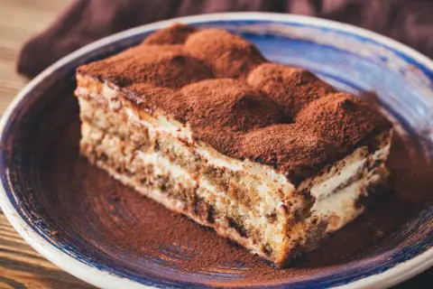 Une part de tiramisu, saupoudrée de cacao, sur une assiette bleue. Un délice qui évoque tous les ingrédients du tiramisu.