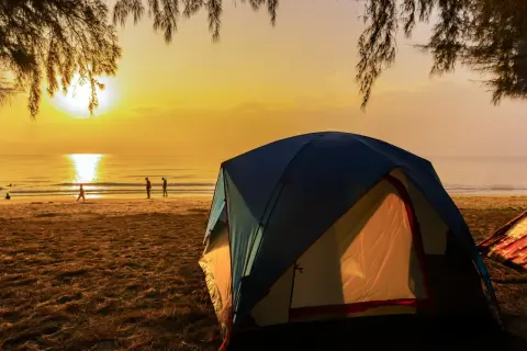 Namiot na polu namiotowym nad morzem przy plaży, gdzie słońce zachodzi, malując niebo na złoto.